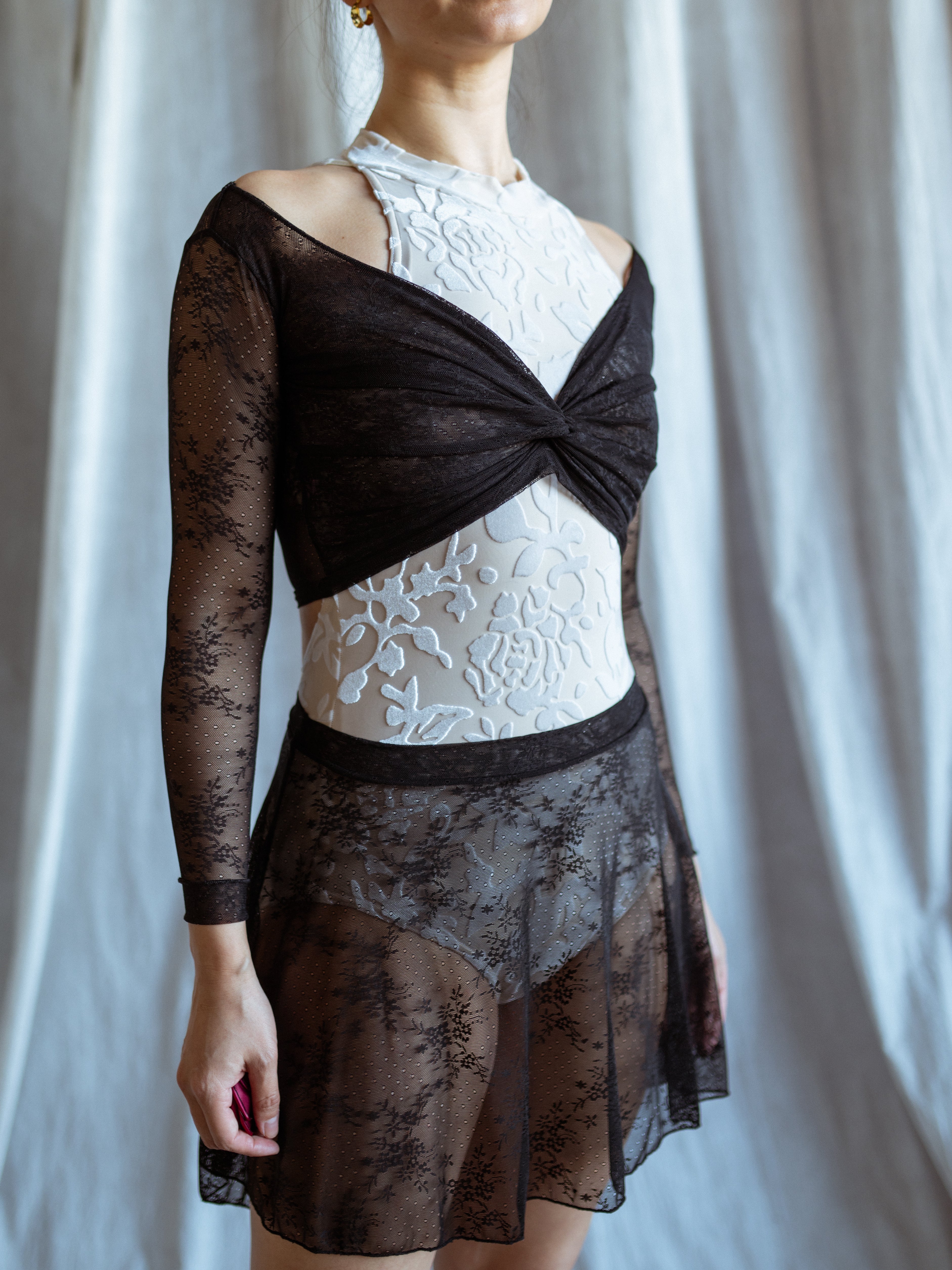 Person wearing a black lave and white leotard black lace skirt against a plain background