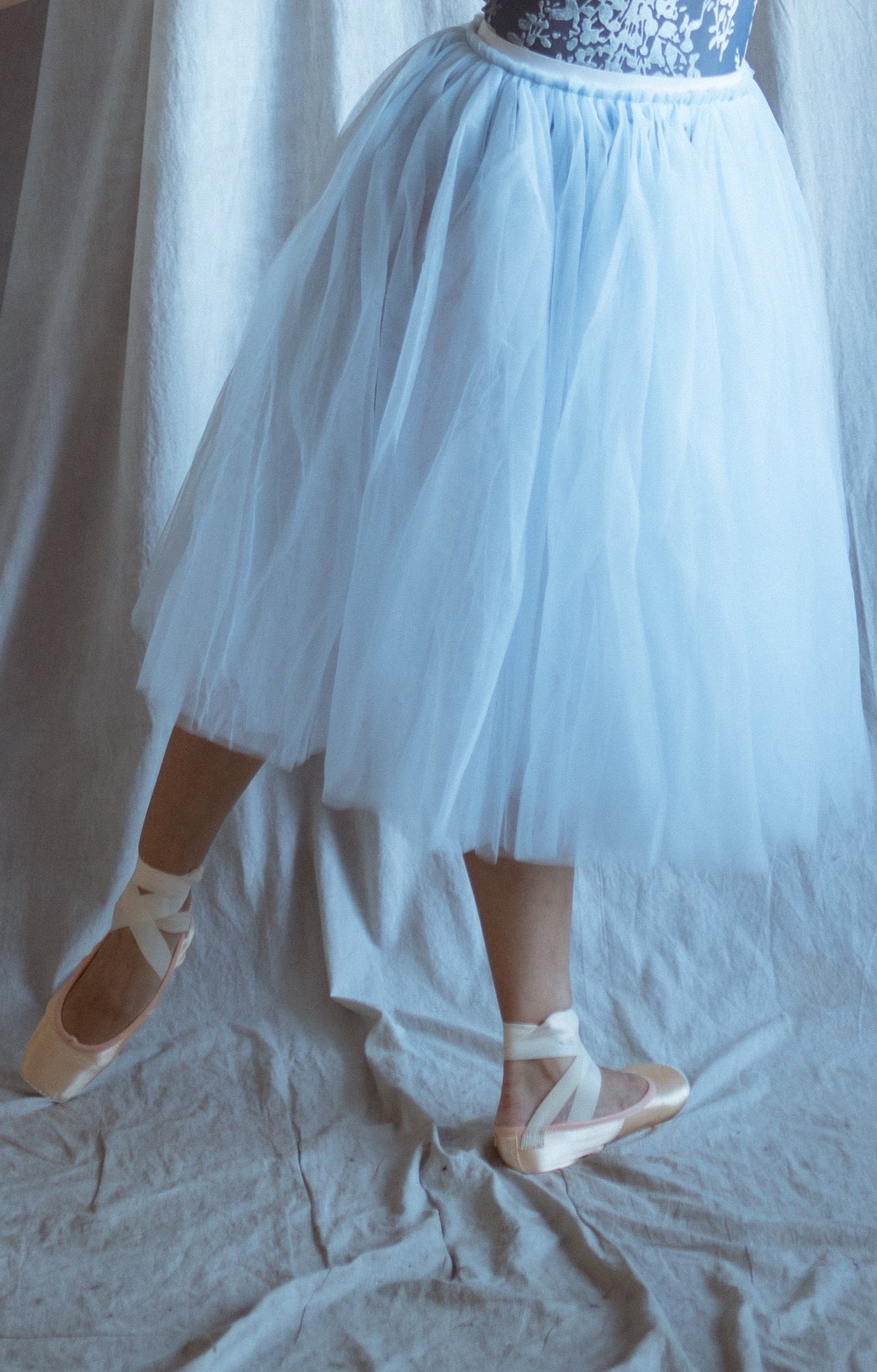 Dancer in a light blue floral velvet leotard and long romantic tutu skirt standing in front of draped fabric