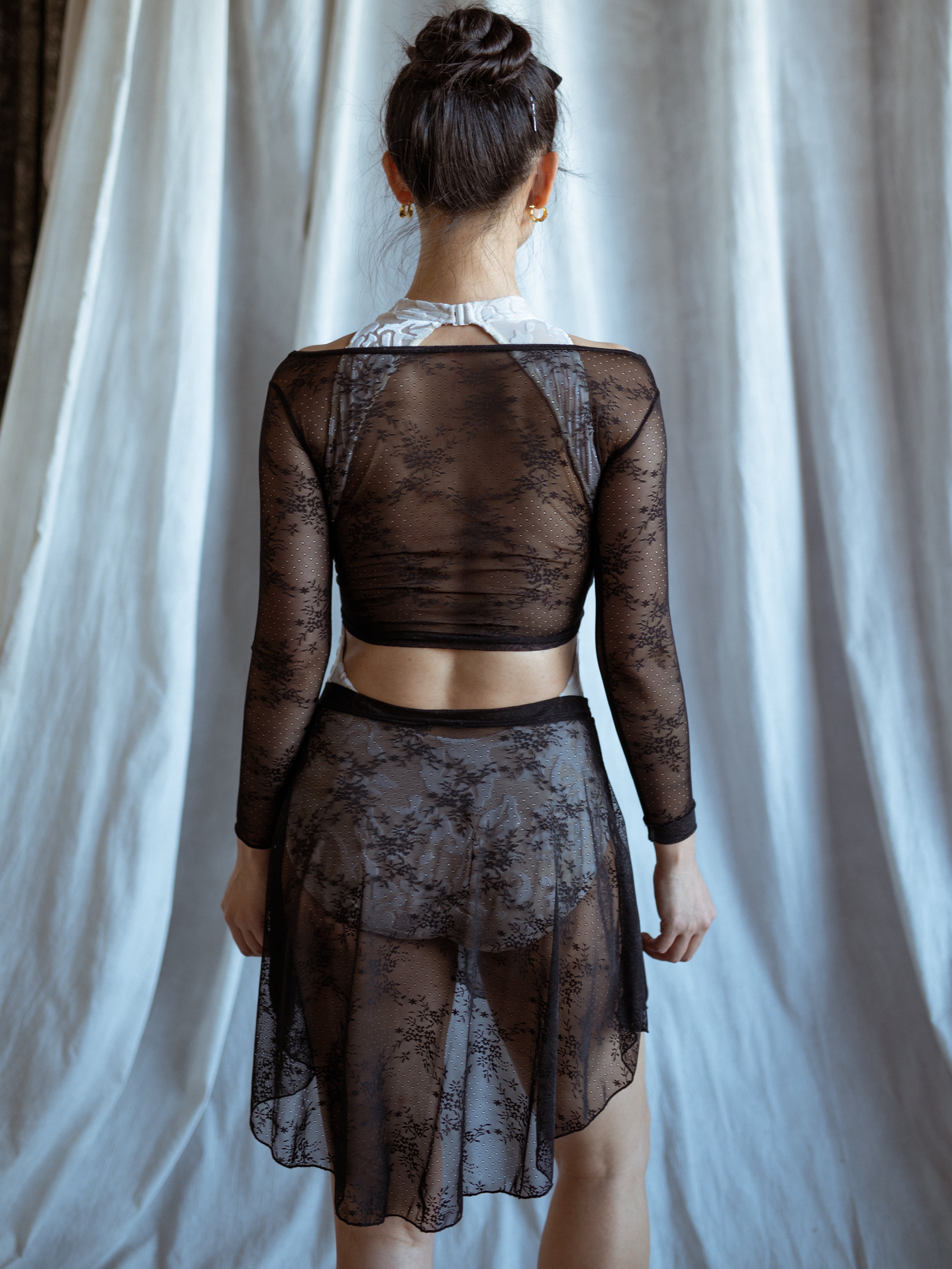 Person wearing a lace black outfit black lace skirt against a white curtain background