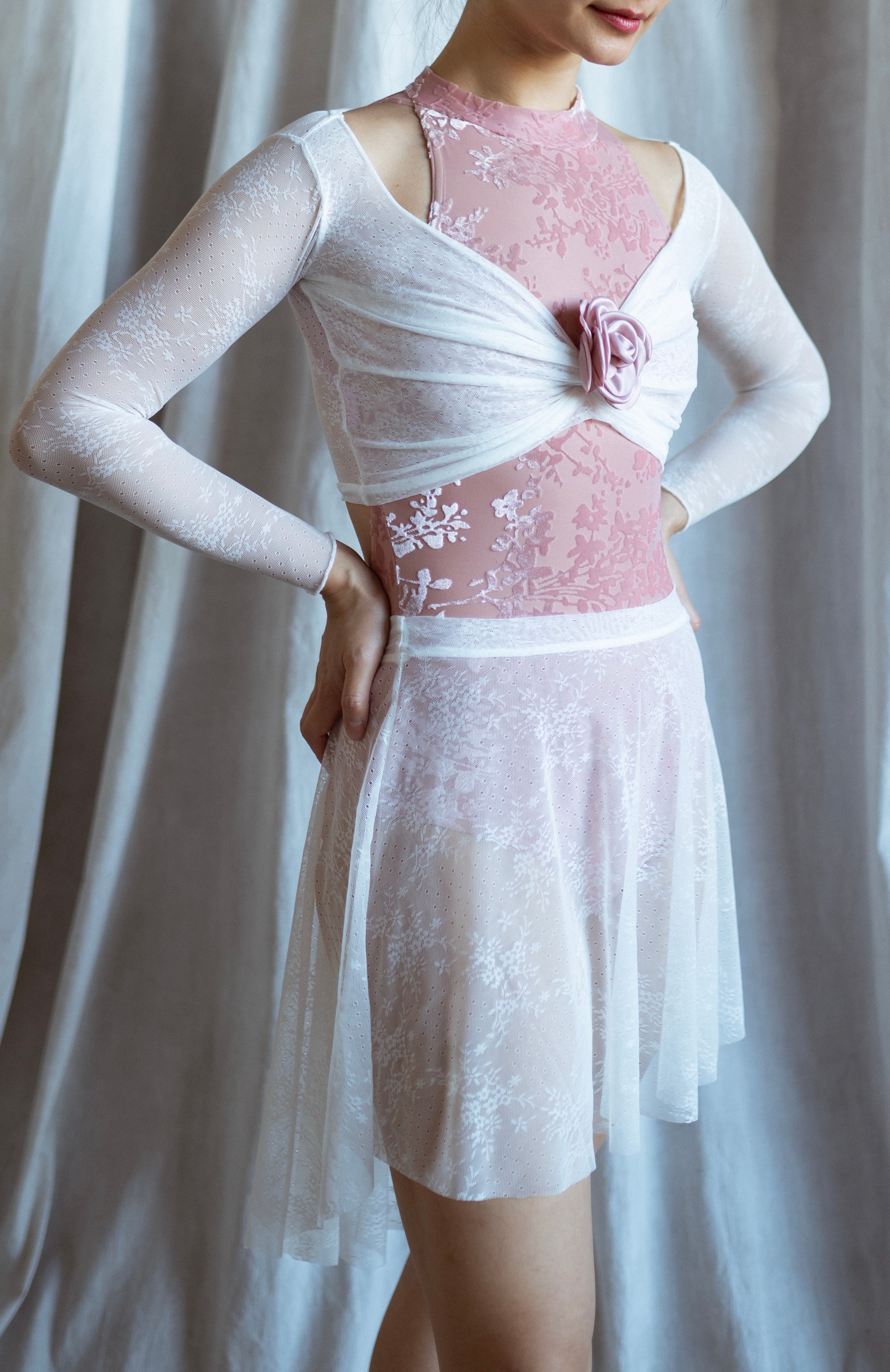 Person wearing a white lace warm up top with a pink floral leotard against a plain background